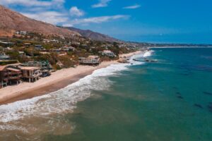 Aerial view of the Malibu coastline with beachfront homes, mountains, and the Pacific Ocean