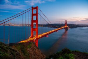 Golden Gate Bridge illuminated at dusk with the San Francisco skyline in the background